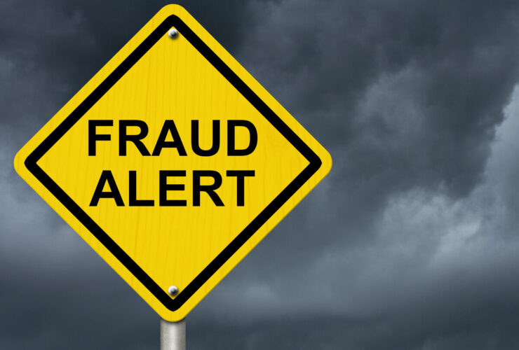 Yellow warning sign reading FRAUD ALERT against stormy sky.
