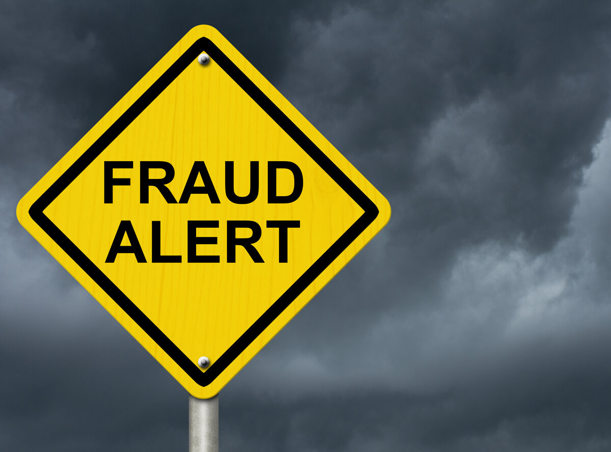 Yellow warning sign reading 'FRAUD ALERT' against stormy sky.